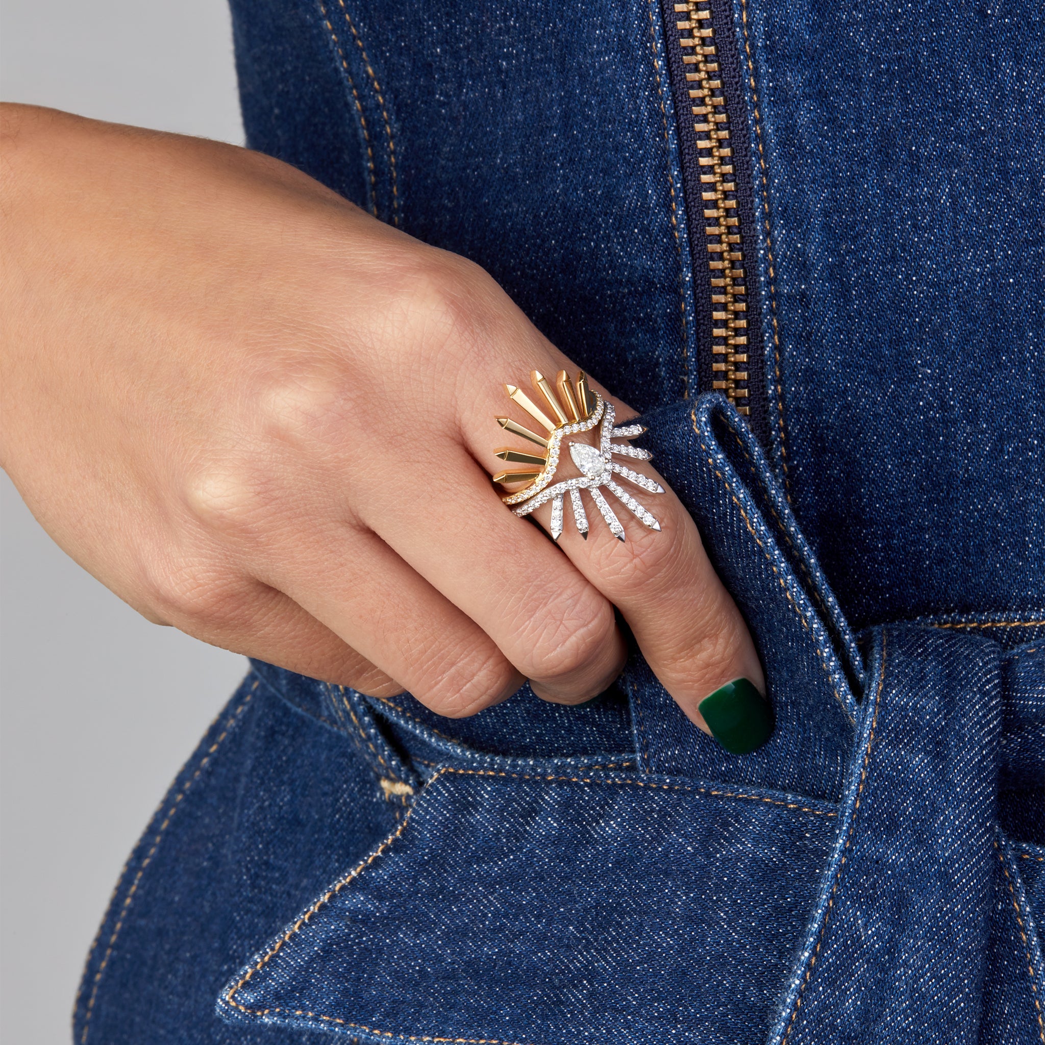 Two rings in yellow and white gold portrayed facing each other on hand model wearing a denim jumpsuit.