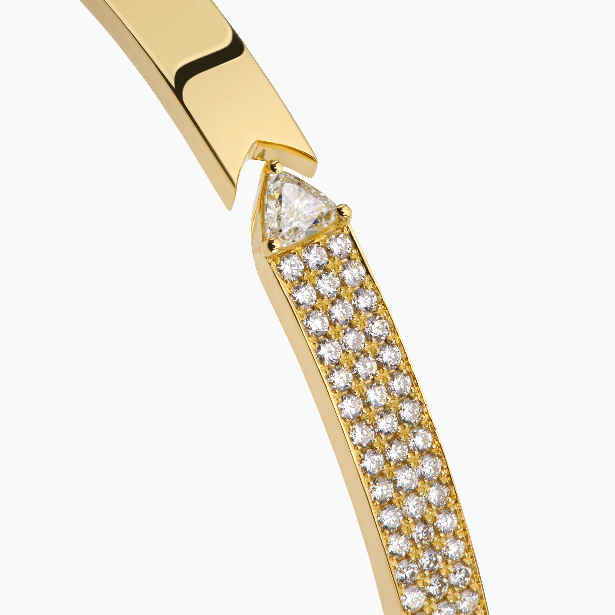 Close up of yellow gold bangle with round brilliant diamonds and trillion displayed against an off white background. 